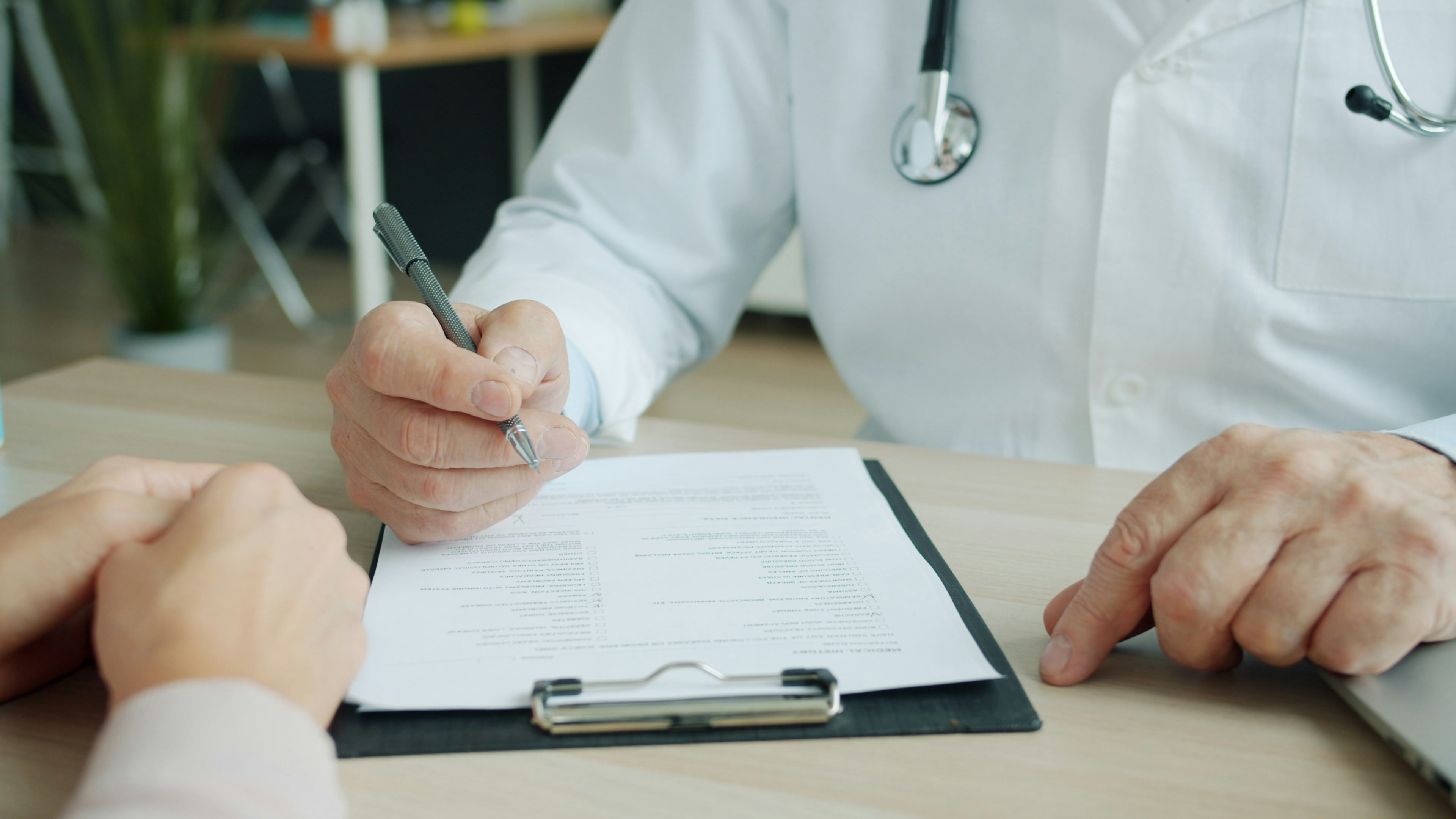 A physician reviewing a clipboard of forms across a desk from a patient
